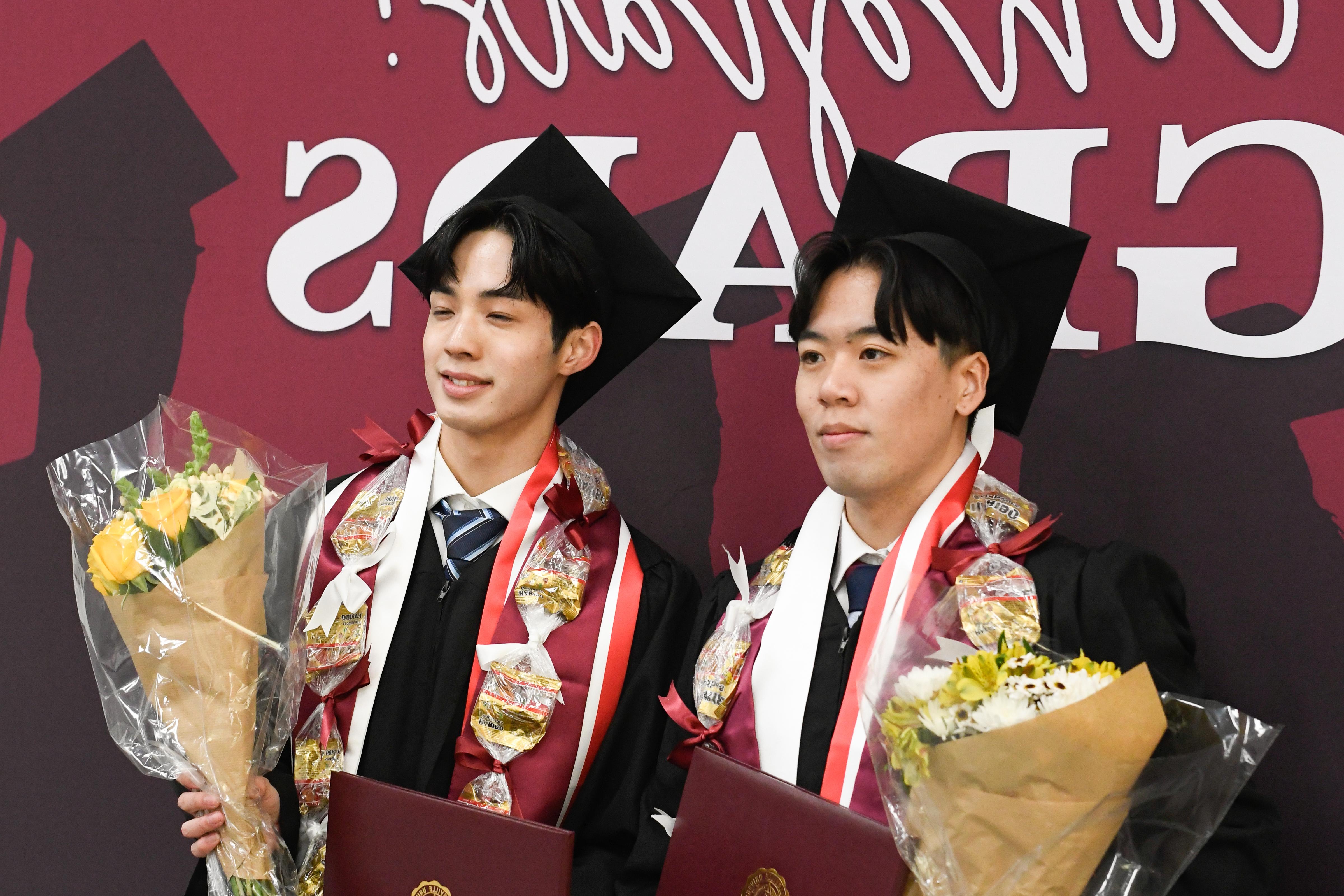 Two people standing in front of a backdrop holding flowers.