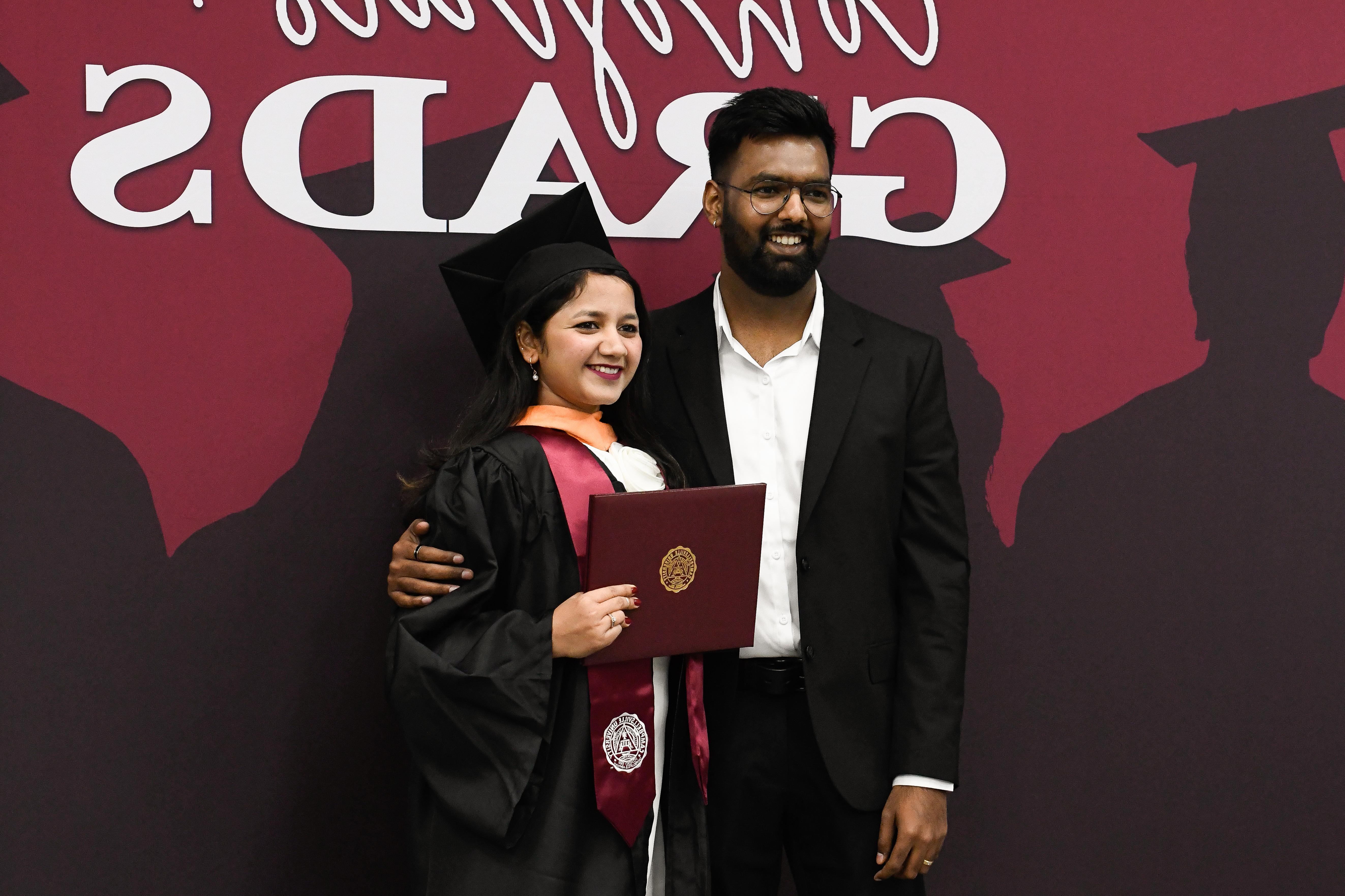 Two people smiling in front of a backdrop.